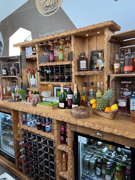 Wooden bar displaying various bottles of spirits, mixers, and fresh fruit garnishes.