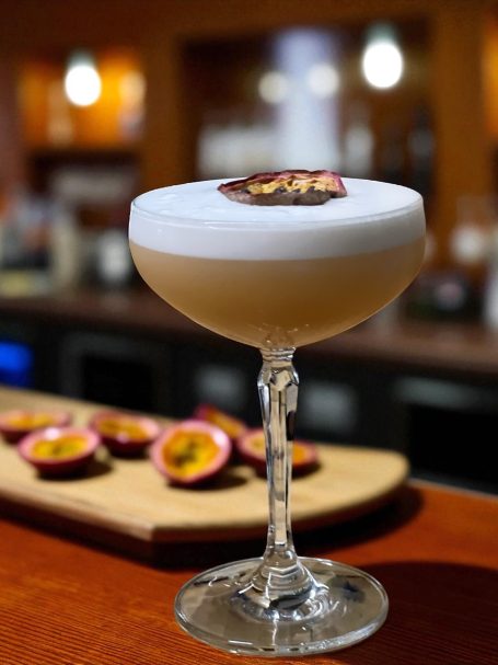 A frothy cocktail garnished with a slice of passion fruit in a stylish glass.